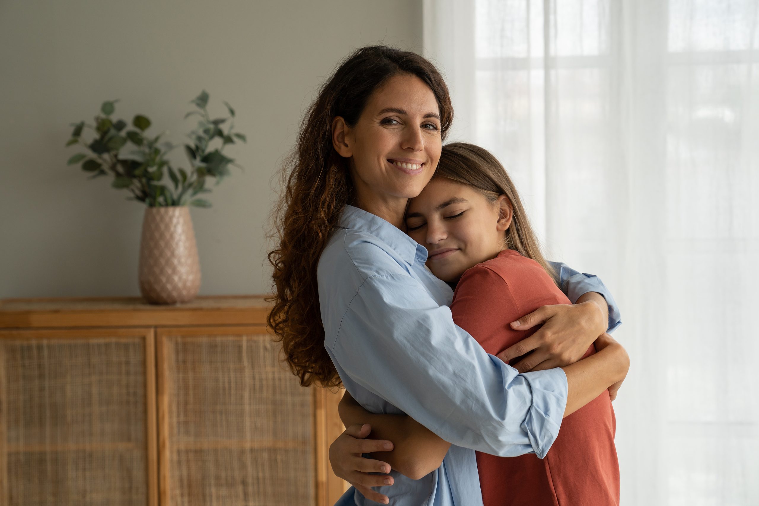 Young loving mother hugging cuddling with teen girl daughter at home and smiling