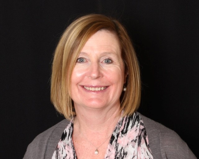 Headshot of Kim Ward. Kim has shoulder length auburn hair and blue eyes.