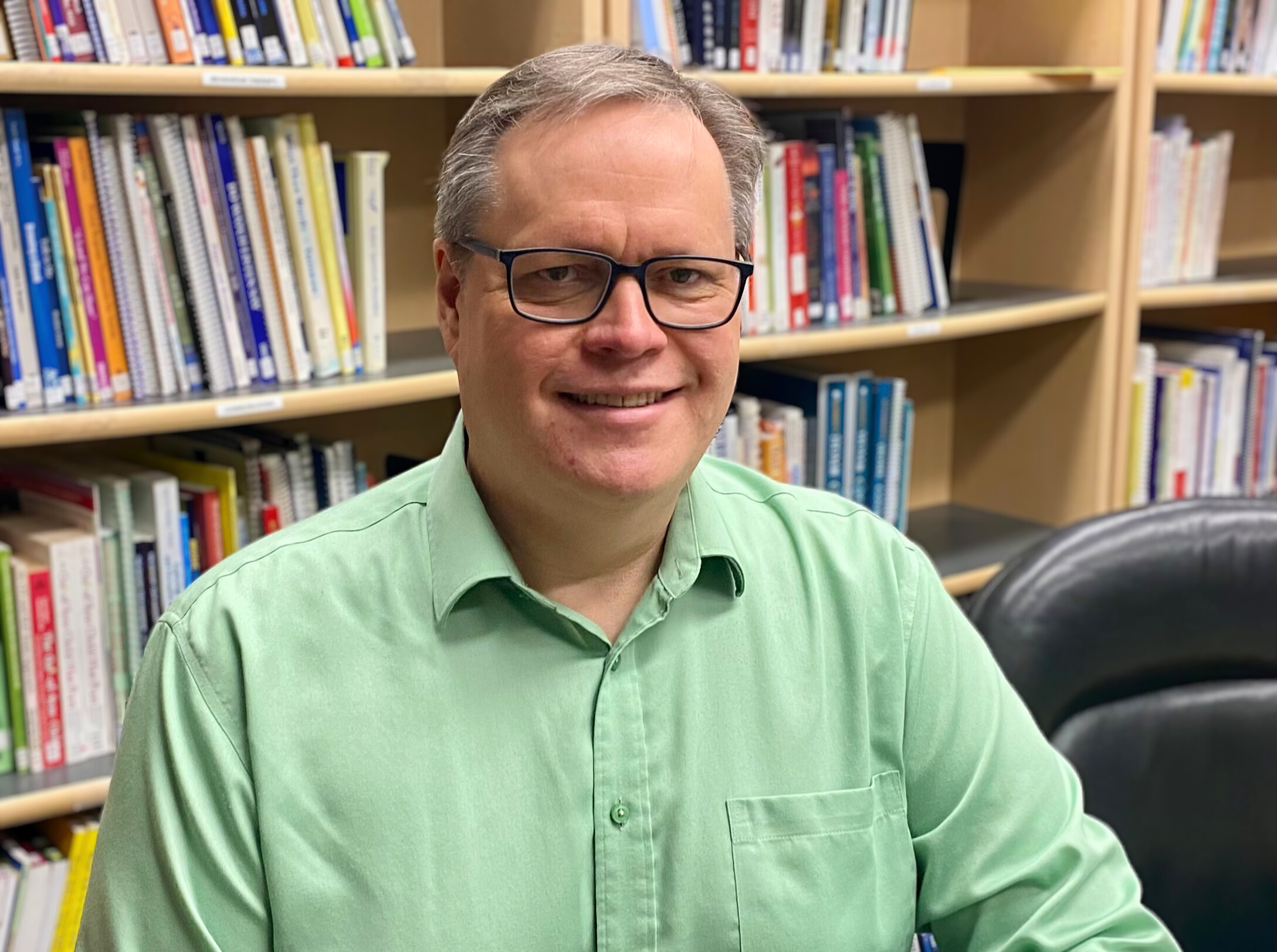 Lyndon, co-chair of the Education Community of Practice, wearing a green button down shirt and glasses.