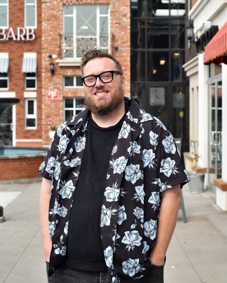 Douglas standing outside wearing glasses and a black and blue floral shirt